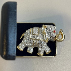 May include: A gold and silver elephant brooch with rhinestones and a red stone for an eye. The brooch is in a black velvet box.