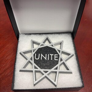 May include: A silver-colored, eight-pointed star with a black center. The center has the word "UNITE" inscribed in white.