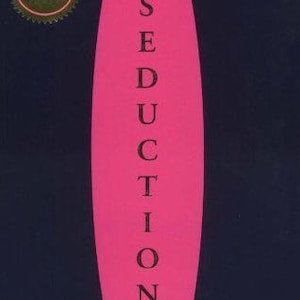 May include: A book titled The Art of Seduction by Robert Greene with a dark navy blue cover featuring a large, vertical, hot pink oval in the centre. The title is printed in black capital letters stacked vertically. A gold circular seal is at the top left.