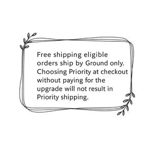 Op de afbeelding: Een rechthoekig kader bestaande uit dunne zwarte lijnen met decoratieve bladaccenten in de linker bovenhoek en rechter onderhoek. De tekst binnenin luidt: Free shipping eligible orders ship by Ground only. Choosing Priority at checkout without paying for the upgrade will not result in Priority shipping.
