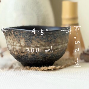 Op de afbeelding: Een donkerbruine en zwarte keramische kom met een textuurrijke, gevlekte afwerking en horizontale groefdetails. De kom is voorzien van witte tekst die een diameter van 11,43 cm, een hoogte van 6,35 cm en een inhoud van 300 ml aangeeft.