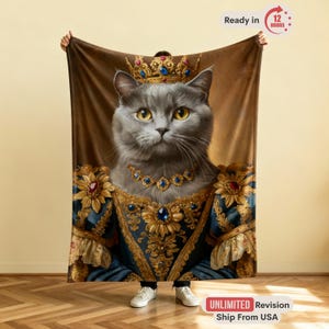May include: A plush blanket featuring a regal portrait of a gray cat adorned with a golden crown and jewelry. The cat is dressed in a blue and gold gown. The blanket has a brown background.