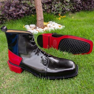 May include: A pair of ankle boots featuring a glossy black leather upper with a square toe and a vibrant red heel and back panel. The boots have black laces and a matching black and red sole with a textured black tread on the bottom.