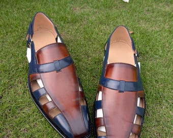 May include: A pair of closed-toe sandals featuring a two-tone design with a smooth brown leather center panel and dark blue leather accents along the sides and heel. The footwear includes cut-out side panels, a square toe, and a buckle strap.