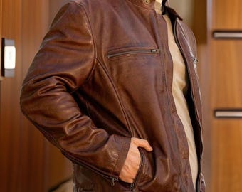May include: A brown leather jacket with a zipper closure and two pockets on the front. The jacket has a stand-up collar and a slightly distressed look.