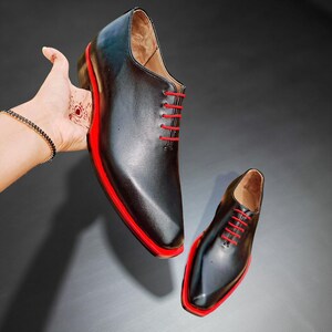 May include: Black leather dress shoes with red soles and red laces. The shoes have a classic design with a modern twist, featuring a sleek silhouette and bold colour accents. A stylish choice for formal occasions.