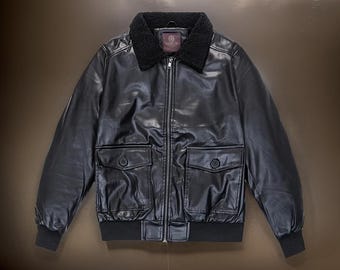 May include: A black leather bomber jacket with a faux fur collar and zipper closure. The jacket has two large pockets on the front and a ribbed knit waistband and cuffs.