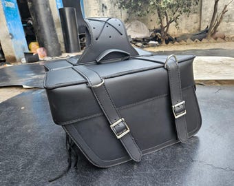 May include: Black motorcycle saddlebag with silver buckles and straps. The bag has a handle on top and a backrest. The bag is made of a smooth, leather-like material. The bag is designed to be mounted on the side of a motorcycle.