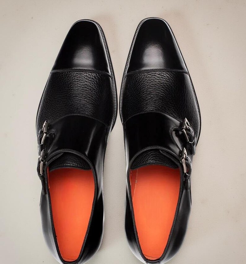 May include: A pair of black leather dress shoes with a textured midsection and silver buckles. The shoes have a glossy finish and orange insoles, showcasing a classic design.