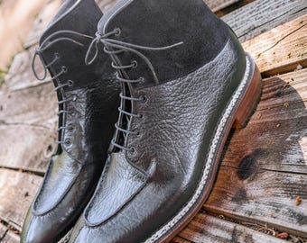 May include: A pair of dark charcoal ankle boots featuring a textured, pebbled leather lower section and a smooth suede upper shaft. The boots have a lace-up front with matching dark laces, a stitched apron toe, a thick welt, and a stacked wooden heel.