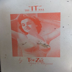 May include: Vintage advertisement for "The IT Bra" by Tre-Zúr, styled in Hollywood. The image features a red and white illustration of a woman wearing the bra, with her arms raised. The text is in red.