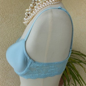 May include: A light blue bra with lace trim on a white mannequin. The bra has adjustable straps and a smooth, seamless cup.