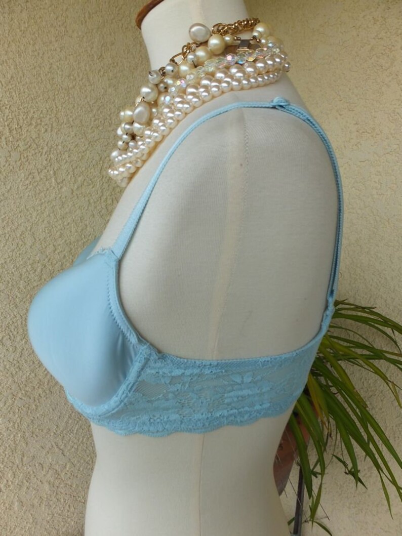 May include: A light blue bra with lace trim on a white mannequin. The bra has adjustable straps and a smooth, seamless cup.