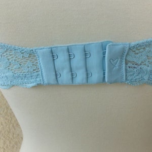 May include: A light blue bra with a lace design and a hook and eye closure. The bra has three hook and eye settings.