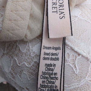 K&ouml;nnte beinhalten: Ein wei&szlig;es Spitzen-BH-Etikett mit dem Text "Victoria's Secret Dream Angels lined demi/demi doubl&eacute; made in China/fabriqu&eacute; en Chine/hecho en China/fabbricato in Cina/中国制造 34DDD/F75"