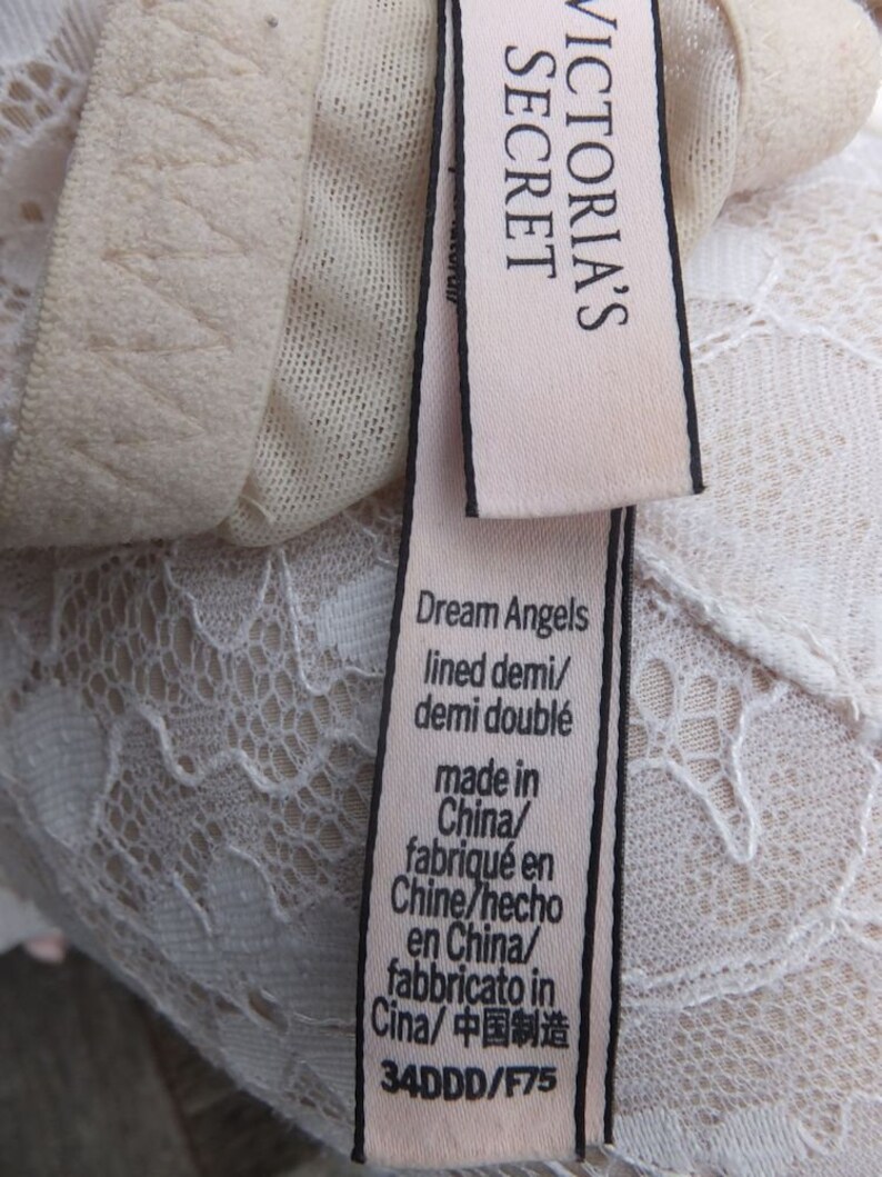K&ouml;nnte beinhalten: Ein wei&szlig;es Spitzen-BH-Etikett mit dem Text "Victoria's Secret Dream Angels lined demi/demi doubl&eacute; made in China/fabriqu&eacute; en Chine/hecho en China/fabbricato in Cina/中国制造 34DDD/F75"