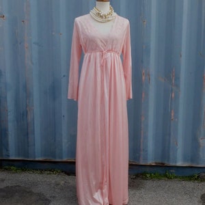 May include: A long, pink satin robe with lace detailing and a tie at the waist. The robe is on a mannequin wearing a pearl necklace.