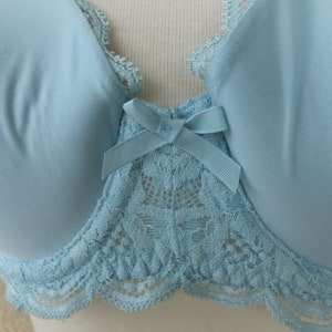 May include: A light blue bra with lace trim and a bow in the centre. The bra has a delicate floral lace pattern.