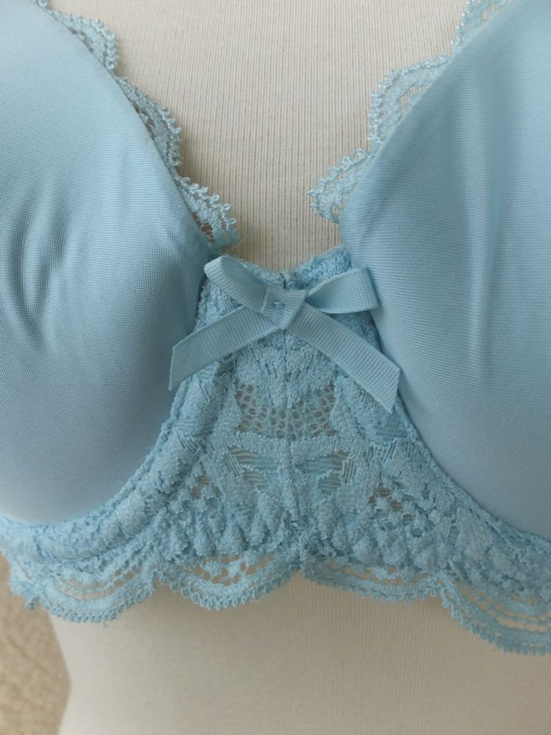 May include: A light blue bra with lace trim and a bow in the centre. The bra has a delicate floral lace pattern.