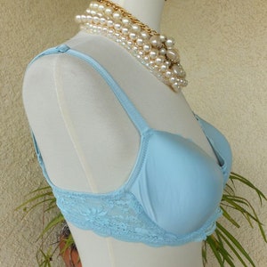 May include: A light blue lace bra with adjustable straps. The bra is on a white mannequin with a pearl necklace.
