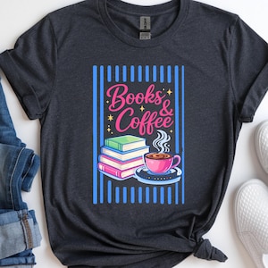 May include: Dark gray t-shirt with a graphic that says "Books & Coffee." The graphic features a stack of books, a steaming coffee cup, and a blue and pink color scheme. The shirt is paired with blue jeans and white slip-on shoes.