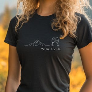 May include: A black t-shirt featuring a white outline of mountains and two wine glasses clinking, with the text "WHATEVER." underneath.