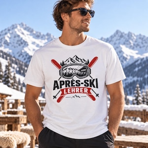 Op de afbeelding: Een wit T-shirt met korte mouwen en een zwart-rode grafische print. Het ontwerp toont gekruiste ski's, een skibril met een reflectie van bergen en de tekst APRÈS-SKI LEHRER in dikke zwarte en rode letters op de voorzijde.