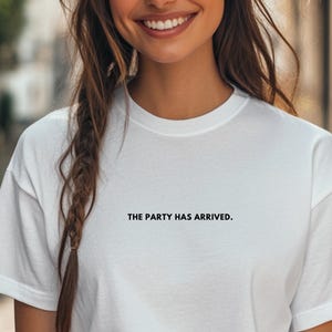 Könnte beinhalten: Weißes T-Shirt mit dem Aufdruck "THE PARTY HAS ARRIVED." in Schwarz.