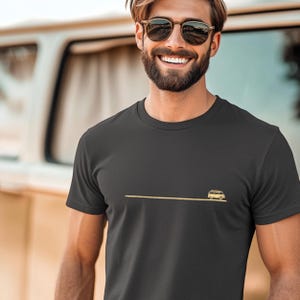 Könnte beinhalten: Ein schwarzes T-Shirt mit einer kleinen, gelben Grafik eines Vintage-Vans, der auf einer Straße fährt.