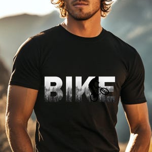 Peut inclure: T-shirt noir avec le mot "BIKE" en lettres blanches. Le mot "BIKE" intègre une silhouette de cycliste de montagne et une scène de forêt.