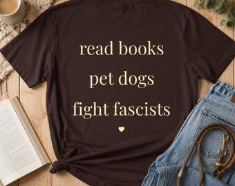 May include: A dark brown short-sleeve t-shirt featuring the light yellow text "read books", "pet dogs", and "fight fascists" stacked vertically, followed by a small light yellow heart symbol centered at the bottom of the graphic.