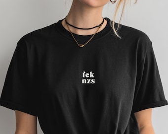 May include: Black t-shirt with the text "fek nzs" in white, centered on the chest. The shirt has a crew neck and short sleeves. The model is wearing a black choker and a gold necklace.