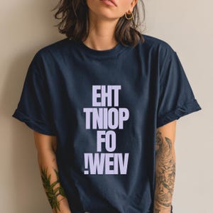 Könnte beinhalten: Marineblaues T-Shirt mit dem Text "EHT TNIOF FO !WEIV" in hellem Lila. Das Shirt hat kurze Ärmel und eine lockere Passform. Der Text ist vertikal gestapelt und erzeugt ein auffälliges Grafikdesign.