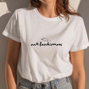 May include: White t-shirt with a black graphic of a mouse and the word "antifaschismaus" in a handwritten font. The shirt has short sleeves and a crew neck.