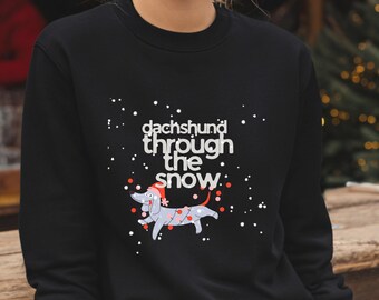 May include: Black sweatshirt with the text "dachshund through the snow" and a cartoon dachshund wearing a Santa hat and Christmas lights. White snowflakes are scattered around the design.