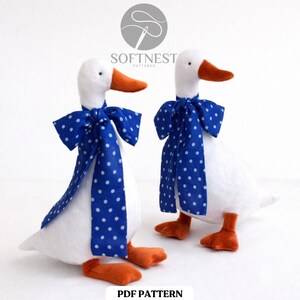 May include: Two white plush goose figures with orange beaks and feet, wearing blue polka dot bow ties. The text "SOFTNEST PATTERNS" is above the geese. The text "PDF PATTERN" is below the geese.
