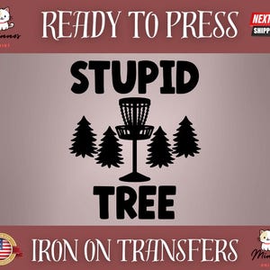 May include: A black graphic design featuring a disc golf basket and pine trees, with the words "STUPID TREE" in bold letters. The image also includes the text "READY TO PRESS" and "IRON ON TRANSFERS".