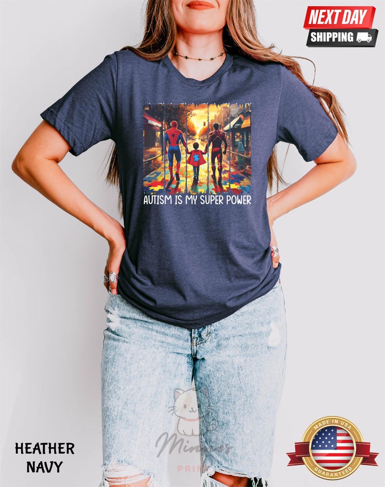 May include: A navy blue t-shirt with a graphic of three superheroes walking on a puzzle piece sidewalk. The text "AUTISM IS MY SUPER POWER" is printed below the graphic.