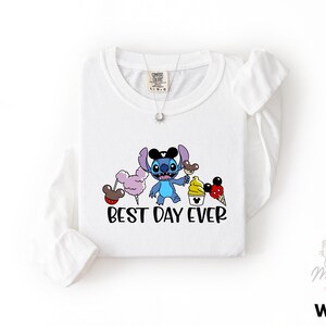 A white long-sleeved t-shirt with a graphic design featuring a cartoon character and the text "BEST DAY EVER".