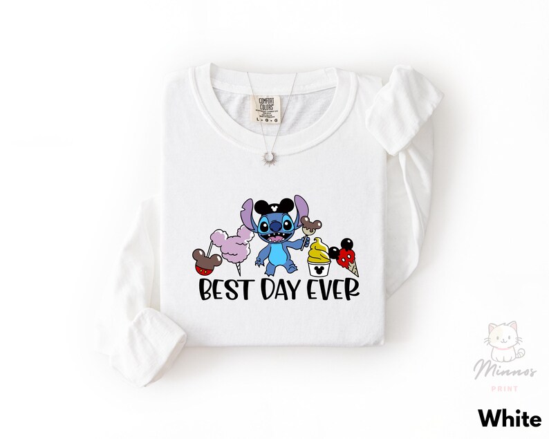 A white long-sleeved t-shirt with a graphic design featuring a cartoon character and the text "BEST DAY EVER".