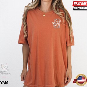 a woman wearing a red t-shirt with the text "Athletic Social Moms Club" printed on it.