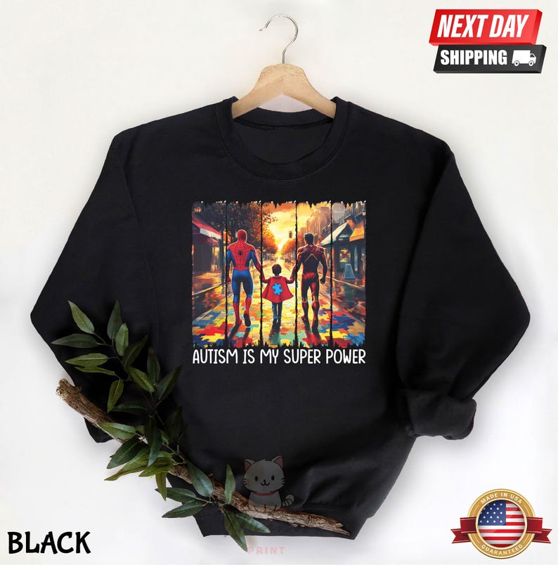 May include: Black sweatshirt with a graphic of three figures walking on a street with a puzzle piece pattern on the ground. The figures are wearing superhero costumes. The text "Autism is my super power" is printed below the graphic.