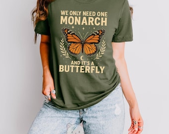 Peut inclure: T-shirt vert militaire avec un motif de papillon monarque et le texte "WE ONLY NEED ONE MONARCH AND IT'S A BUTTERFLY." Le papillon est orange et noir. Fabriqué aux États-Unis.