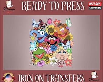 Pode incluir: Transfer para passar a ferro com um design colorido de personagens dos Muppets, rodeados por flores e borboletas. O texto "READY TO PRESS" está no topo e "IRON ON TRANSFERS" na parte inferior.