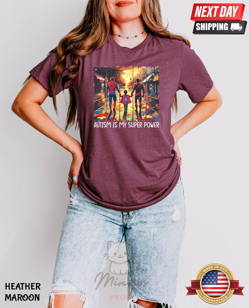 May include: A heather maroon t-shirt with a graphic of three figures walking on a street with a puzzle piece pattern on the ground. The text "AUTISM IS MY SUPER POWER" is printed below the graphic.