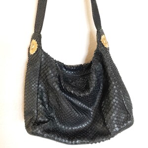 May include: Black leather handbag with a snakeskin pattern and gold accents. The bag has a single strap and a zipper closure.