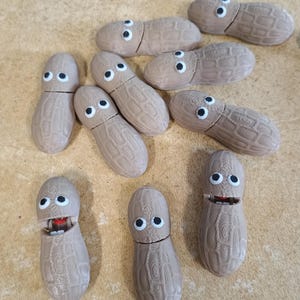 May include: A collection of 10 brown peanut-shaped toys with googly eyes and open mouths. Some of the peanuts have teeth and others have a red tongue.