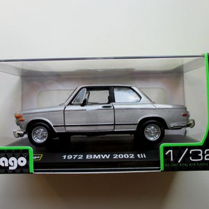 Op de afbeelding: Zilverkleurig modelauto van een BMW 2002 tii uit 1972 in een transparante display. Het model is schaal 1:32 en heeft zwarte banden en een zwart interieur. De verpakking bevat het Burago-logo en het woord "Classic".