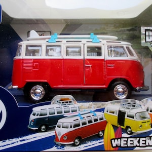 May include: A red and white toy VW bus with a surfboard on top, packaged in a box. The box also displays other colorful toy buses. The packaging includes the text "Maisto" and "Die-Cast with Moving Parts".