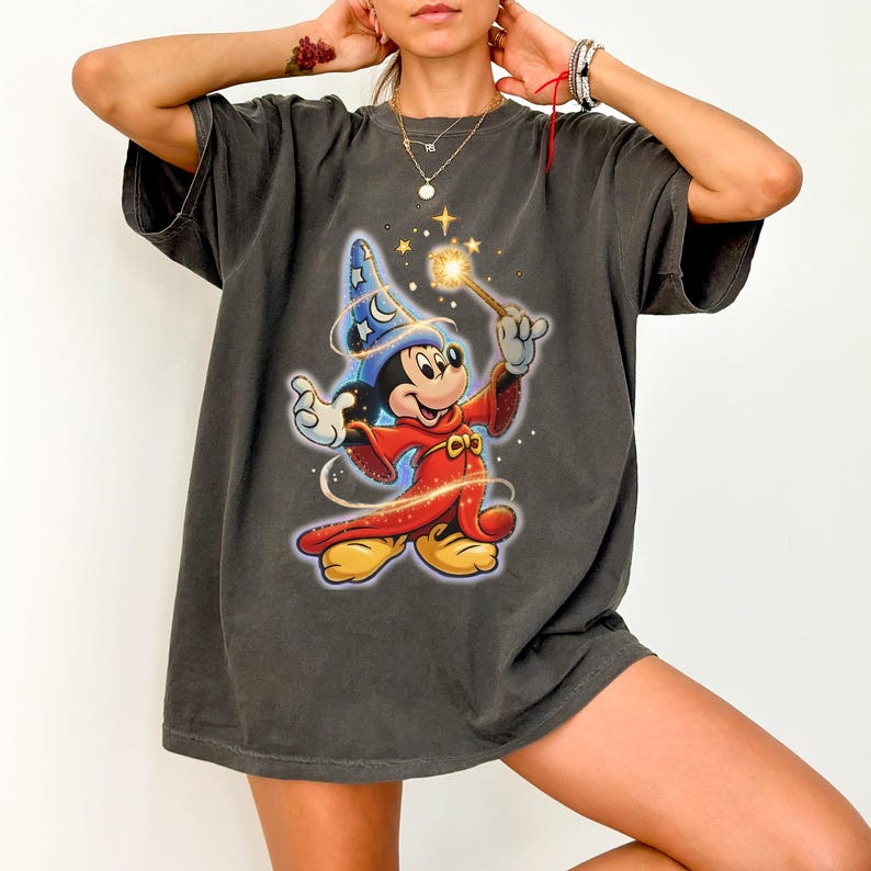 Peut inclure: T-shirt gris fonc&eacute; avec un motif color&eacute; de Mickey Mouse en magicien, tenant une baguette avec une &eacute;toile brillante. Le personnage de dessin anim&eacute; porte un chapeau de magicien bleu et une robe rouge. Le t-shirt a des manches courtes et une coupe d&eacute;contract&eacute;e.